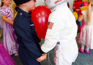Para chłopców tańczy trzymając czerwony balon między sobą
